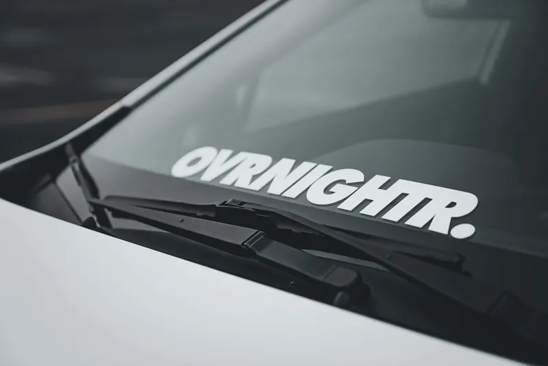 Close-up view of a car windscreen featuring a bold OVRNIGHTR decal, emphasizing modern automotive design.