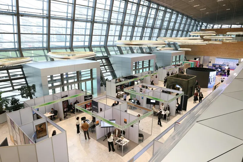 A bustling trade show exhibition inside a modern hall with people networking and exploring booths.